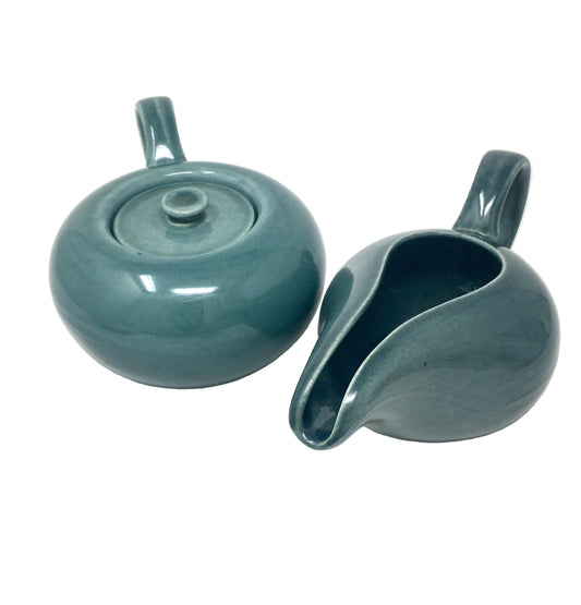 Two teal ceramic items, one with a lid and the other shaped like a boat, on a white background.
